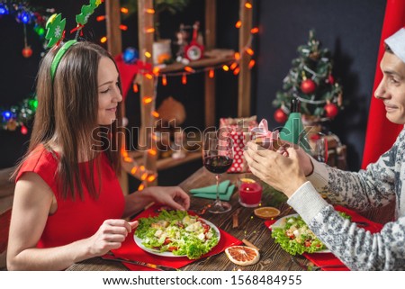 A young beautiful couple of lovers are spending a festive Christmas dinner. Husband makes his wife a surprise giving a new year gift