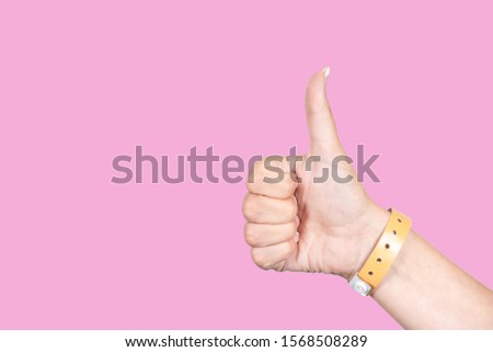Close up side view of beautiful one female hand isolated on pink background. Woman showing thumb up, wrist with rubber orange entrance bracelet. Horizontal color photography.