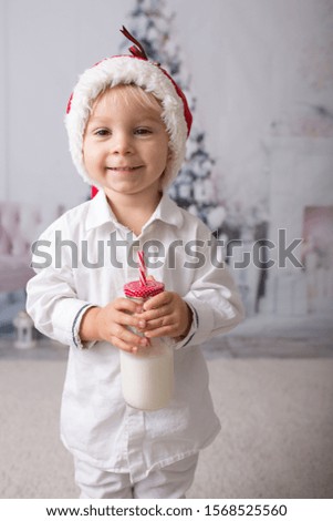 Beautiful toddler boy with red santa hat, holding bottle with milk, drinking, Christmas decoration