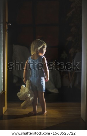 Toddler child, boy, hodling teddy bear, standing in hallway next to the door to bedroom, fairy tale picture