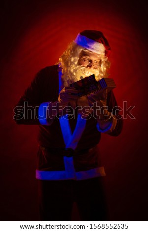 Santa Claus holds a gift box in his hands, looks into it and poses on a dark red background