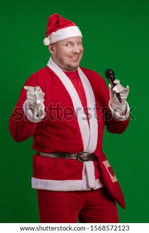 Male actor in a costume of Santa Claus holds a microphone in his hands, sings and poses on a green background