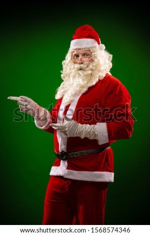 Male actor in a costume of Santa Claus dancing and gesturing, posing on a green background