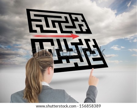 Composite image of businesswoman pointing at holographic maze floating in sky