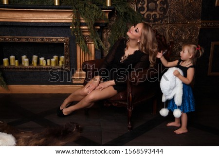 Smiling joyful mom with her daughter near the Christmas tree New Year, Christmas concept play, girl puts on a hat