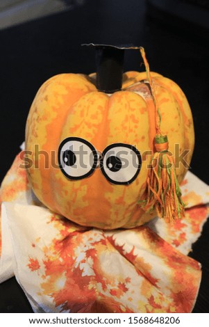 Paper-eyed red pumpkin with a square academic cap and a red tassel on a black background