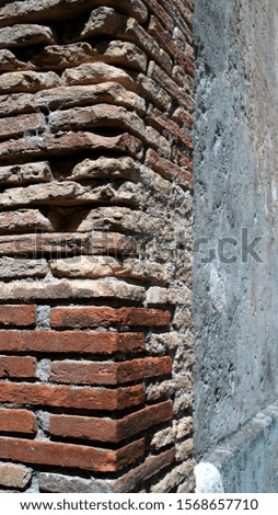 Corner of broken concrete wall and aligned red bricks seen in side perspective, in the sun