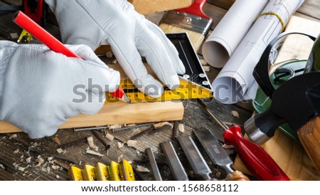 View from above. Carpenter wears protective leather gloves, with the pencil and the carpenter's square draw the line on a wooden board. Construction industry, do it yourself. Wooden work table.