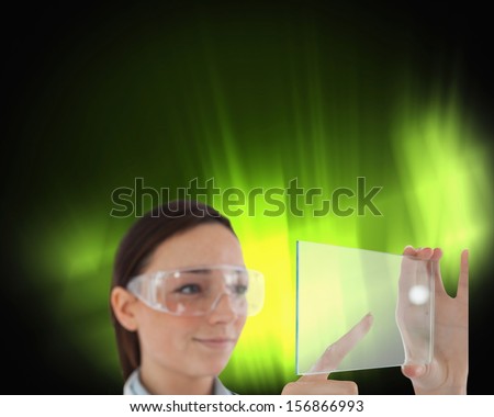 Composite image of brunette doctor in protective glasses holding virtual screen on black background with green glowing inside