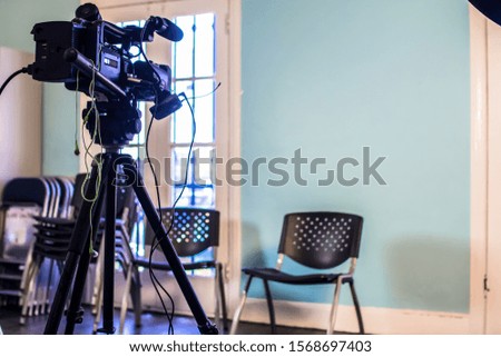 Wide shot of a Professional TV and Cinema production Camcorder HD Camera on set sitting on a tripod recording and filming towards a chair and backdrop