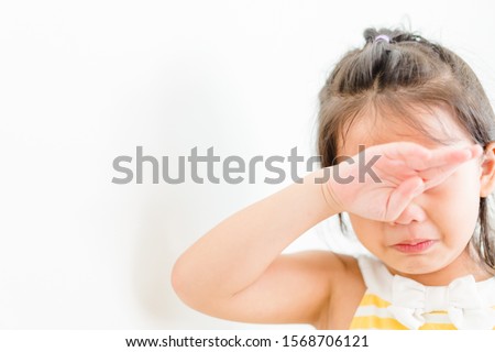 Little girl suffering from eye ache problem and headache before finish cartoon series.Crying crazy kid girl on white wall at home.Kid with attention deficit hyperactivity disorder (ADHD) Royalty-Free Stock Photo #1568706121