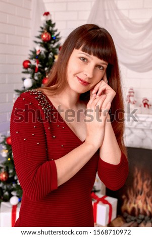 Young attractive brunette girl on the background of fir-tree new year's eve in a beautiful Burgundy dress