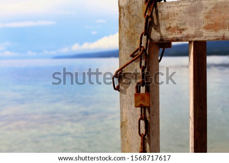 Abstract Minimalist Photography,rusty padlock and iron chain on door made of wooden bars,blurry seascape as background