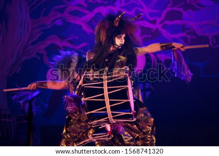 Taiko drummer in a wig and a demon mask performs on stage with drum on a dark background. Demon from Japanese mythology.