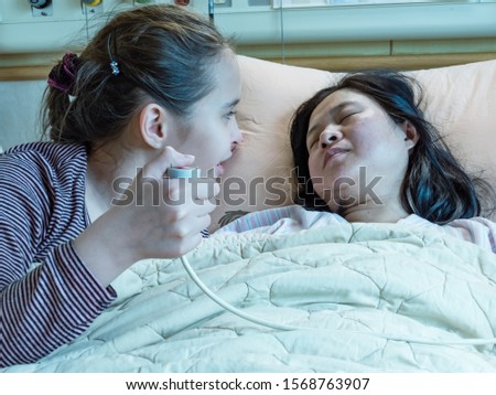 Asian Mother and daughter laying in hosital bed, child pressing nurse call button