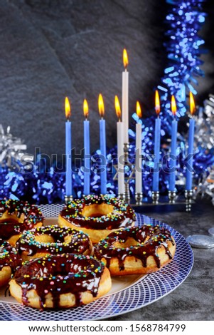 Jewish holiday Hanukkah. Sweet donuts and menorah with burning candles on decorated table.