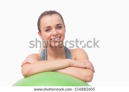 Young ponytailed woman smiling at camera supporting herself with a fitness ball