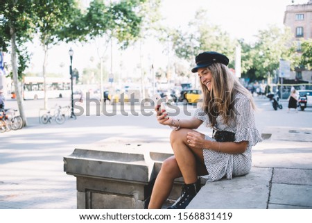Positive hipster girl - lover of travelling and exploring new cities taking rest on Barcelona streets for clicking selfie pictures via cellphone front camera for capture good moment in memory