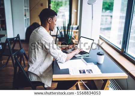 Dark skinned male freelancer working remotely on modern laptop computer with blank screen for internet web advertising, millennial student preparing to exam with web information from netbook