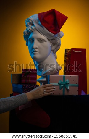 Statue of Apollo Belvedere in a red cap of Santa Claus, gifts boxes and packages, in blue contour light on multi-colored backgrounds. Composition for congratulations.