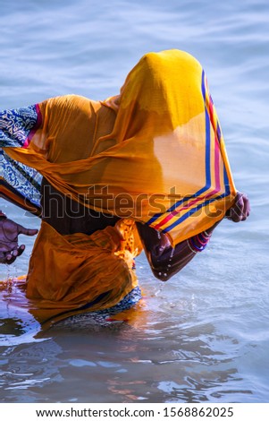 Life on the Ganges: woman in a bright yellow or orange sari bathing in the Ganges as religious ritual. beautiful color contrasts. Varanasi, India.