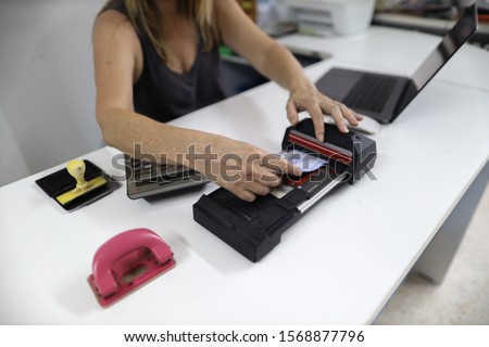 Clear image of female hand inserting  imprinting paper with credit card underneath into old pre-digital credit card imprinter machine white office table background 