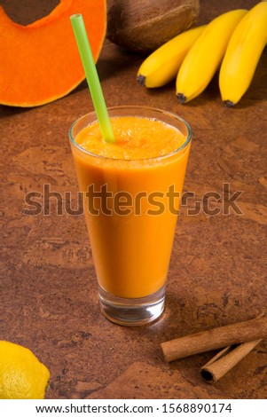 Fresh pumpkin smoothie with bananas in a glass on a brown background. Selected focus.