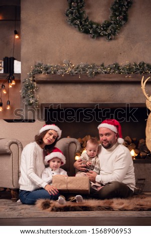 Picture of parents in Santa's cap with two sons sitting on floor by fireplace in room