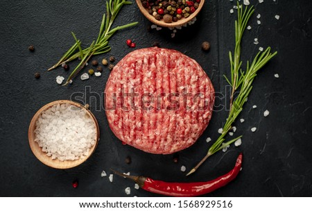 
Raw beef burger cutlets with herbs and spices on a concrete background