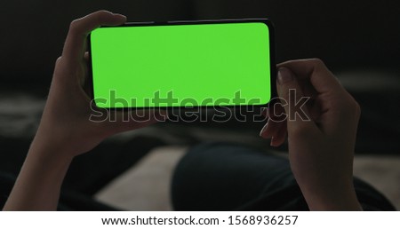 Young woman lying on a couch and using smartphone with horizontal green screen