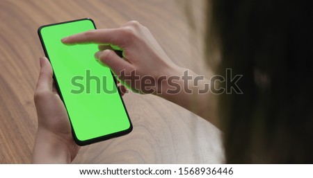 Young woman sitting at a table and using a smartphone with vertical green screen