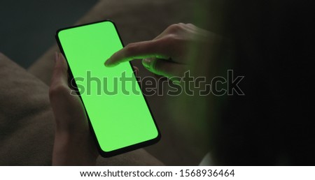 Young woman sitting on a couch and using smartphone with green screen