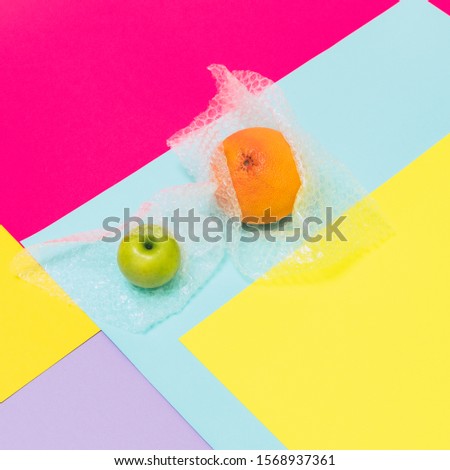 Orange fruit and apple with plastic bubble wrapper on geometric background. Concept of environmental pollution and waste recycling. 