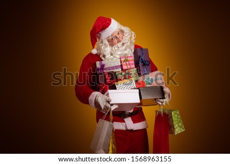 Santa Claus holds a lot of gift boxes and packages in his hands and poses on a yellow background