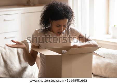 Disappointed african American woman sit on couch in living room feel frustrated with wrong order shopping online, confused biracial female unhappy with parcel unpacking, bad delivery service concept Royalty-Free Stock Photo #1568981662