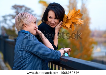 Two girlfriends talking and posing in autumn city park. Beautiful adult woman, blond and brunette.