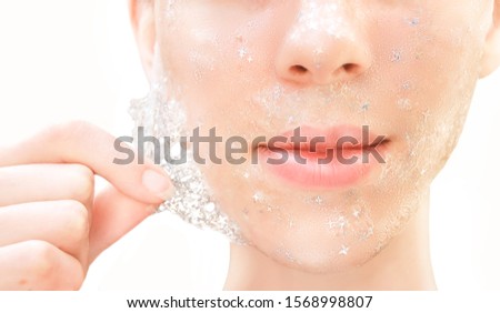 Beautiful young woman with healthy skin removes purifying transparent peel off mask with shiny sparkling star glitter from her face. Trendy cosmetic beauty procedure.Skin care concept. Royalty-Free Stock Photo #1568998807