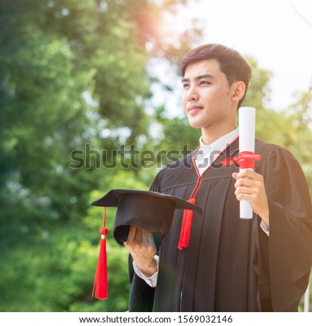 Square image of young Asian man looking ahead with pride, wearing graduation gown, caps and certification. 