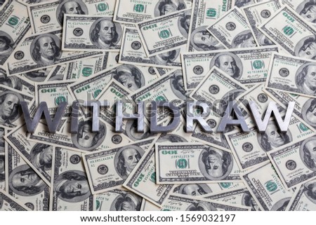 The word WITHDRAW laid with aluminium letters on the US dollar banknotes background - with selective focus
