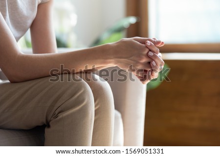 Close up young woman sitting on sofa with folded hands on knees. Thoughtful millennial lady waiting for important news, feeling puzzled, making complicated decision or recollecting memories at home. Royalty-Free Stock Photo #1569051331