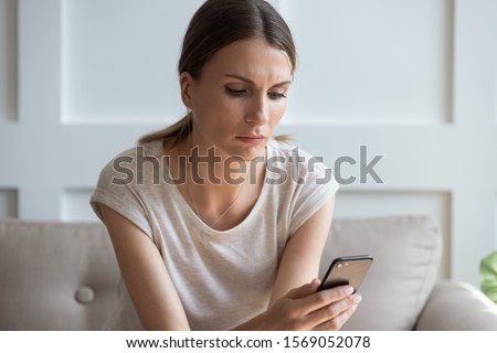 Head shot unhappy thoughtful woman looking at cellphone screen, waiting for call from boyfriend. Pensive millennial lady reading sms or email with bad news, checking social networks, sitting at home. Royalty-Free Stock Photo #1569052078