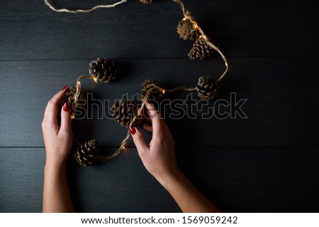 young bright girl with red nails in her hands creates Christmas decorations from cones on a dark wooden background