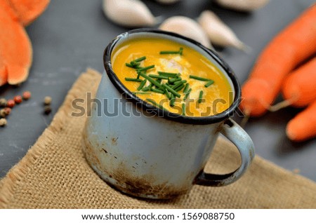 Pumpkin soup with cream and fresh chive in old enamel cup.