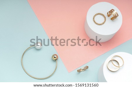Flat lay of golden and pearl bracelet and golden rings collection on pink and green background