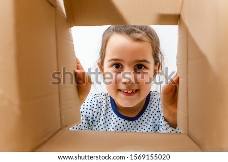 kid girl age 7 year unpacking and opening carton box, and looking inside with surprise