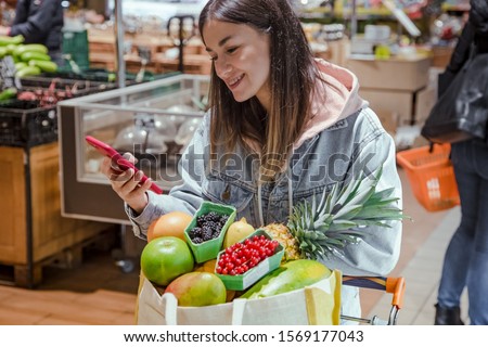 A young woman buys groceries in a supermarket with a phone in her hands. Health food.