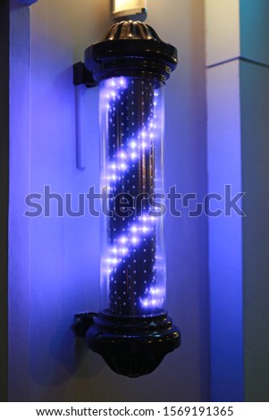 Barber pole turning swirl LED light sign in dark background.