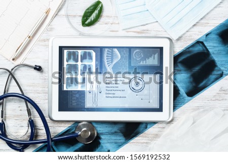 Human genetic research in medical laboratory. Tablet computer with DNA helix structure on screen. Stethoscope, x-ray image and cardiogram on wooden desk. Medical diagnostics and patient genome testing Royalty-Free Stock Photo #1569192532