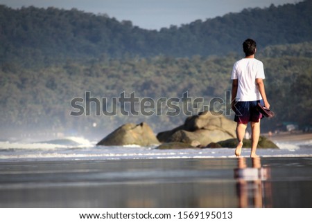 Stock photos, pictures and royalty-free images of Man walking alone on the beach  coast, leaving footprints and reflections on the sand  in peace of mind, enjoying the nature slippers in hands