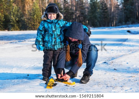 Mom with a young son on a walk. My mother teaches  to ski. Fastens the boy fastening